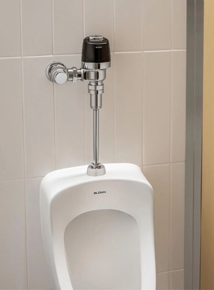 Sloan automatic flushometer installed on a white porcelain urinal, featuring a hygienic and water-efficient design.