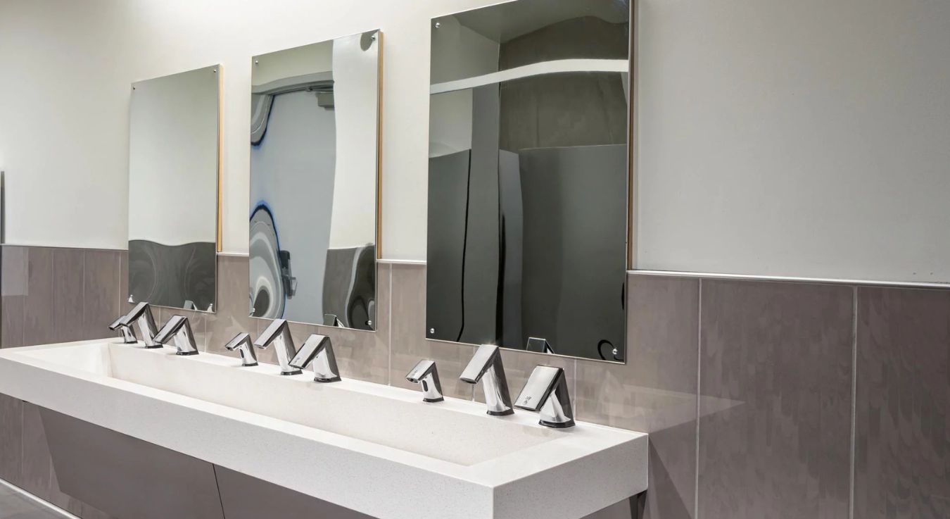 Wide sink counter with Sloan touch-free faucets and rectangular mirrors, designed to promote contactless hygiene in educational environments.