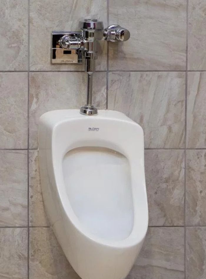 White urinal with Sloan flushometer installed over neutral tiles for a clean, functional, and visually balanced environment.