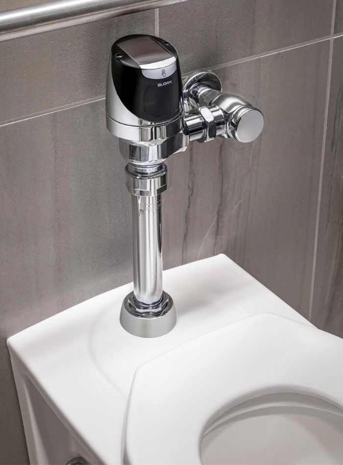 Chrome automatic flushometer installed on a toilet, designed to optimize water use and maintain touch-free hygiene.