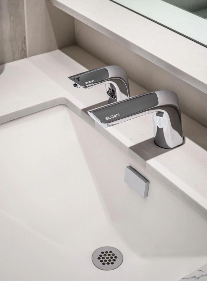 Sink area with modern chrome automatic faucets, integrated into a light marble surface for an elegant and functional look.