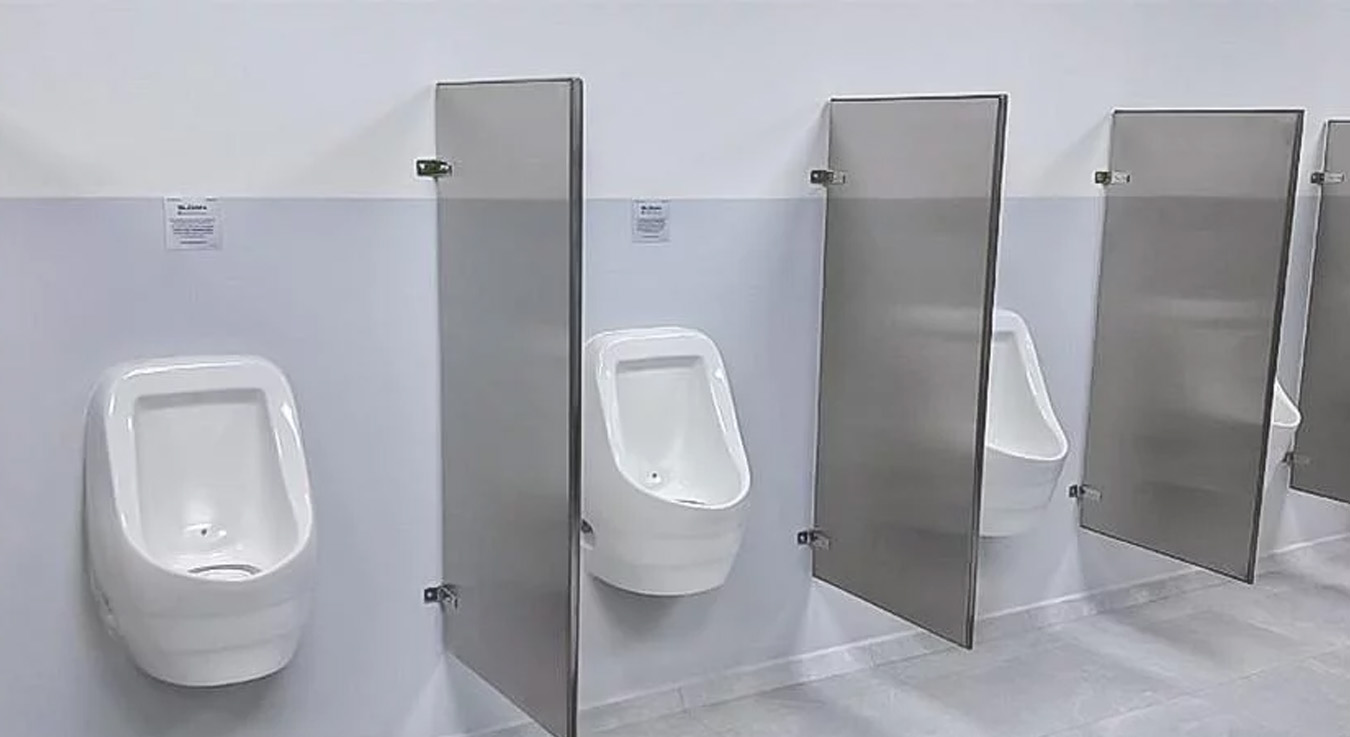 a row of white urinals with metal partitions in a modern public restroom. The space features clean lines and durable materials, prioritizing privacy, hygiene, and functionality in a contemporary setting.