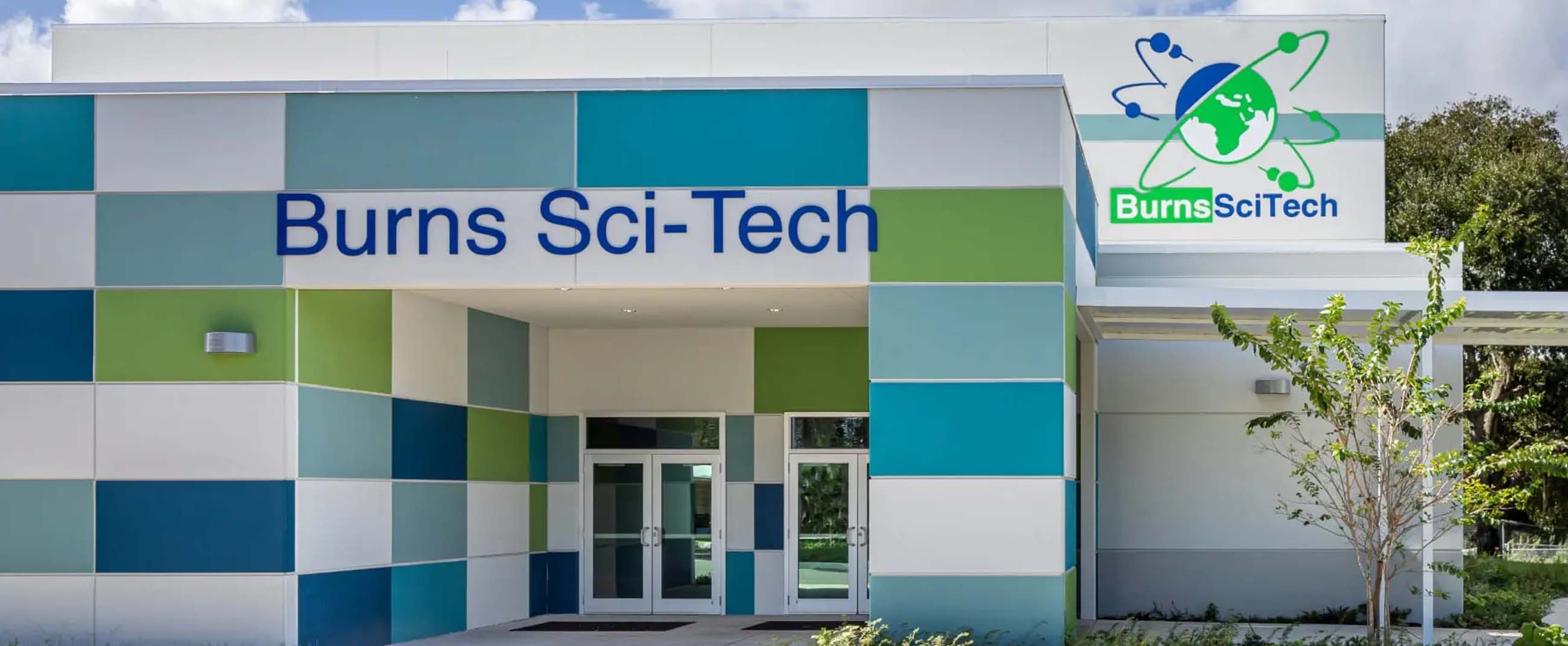 the main entrance of Burns Sci-Tech Charter School, an educational institution known for its focus on Science, Technology, Engineering, Art, and Mathematics (STEAM). The modern architecture, featuring panels in blue, green, and white, symbolizes the school’s innovative and sustainable approach to learning.