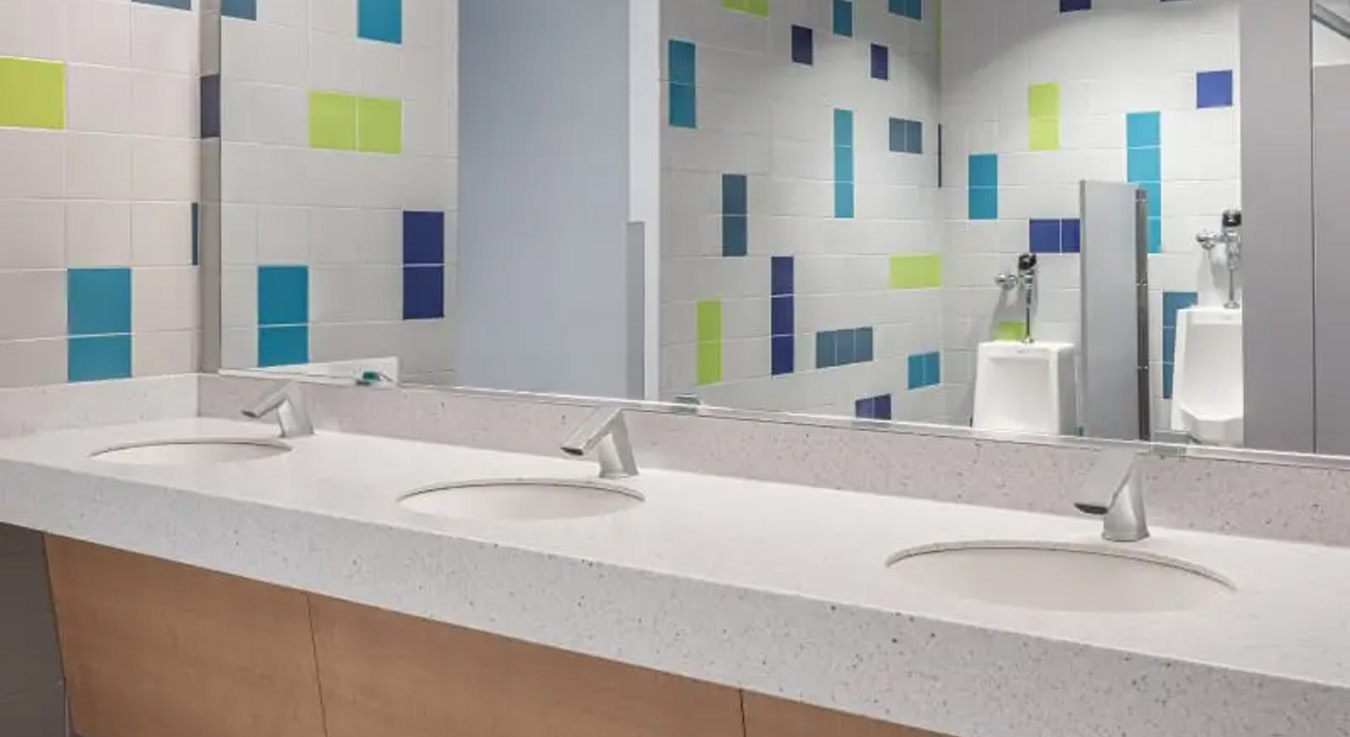 the sink area at Burns Sci-Tech Charter School, featuring Sloan touch-free faucets that enhance hygiene and water efficiency. The vibrant color palette —blue, green, and white— reflects the school’s visual identity and contributes to a bright, modern learning environment.