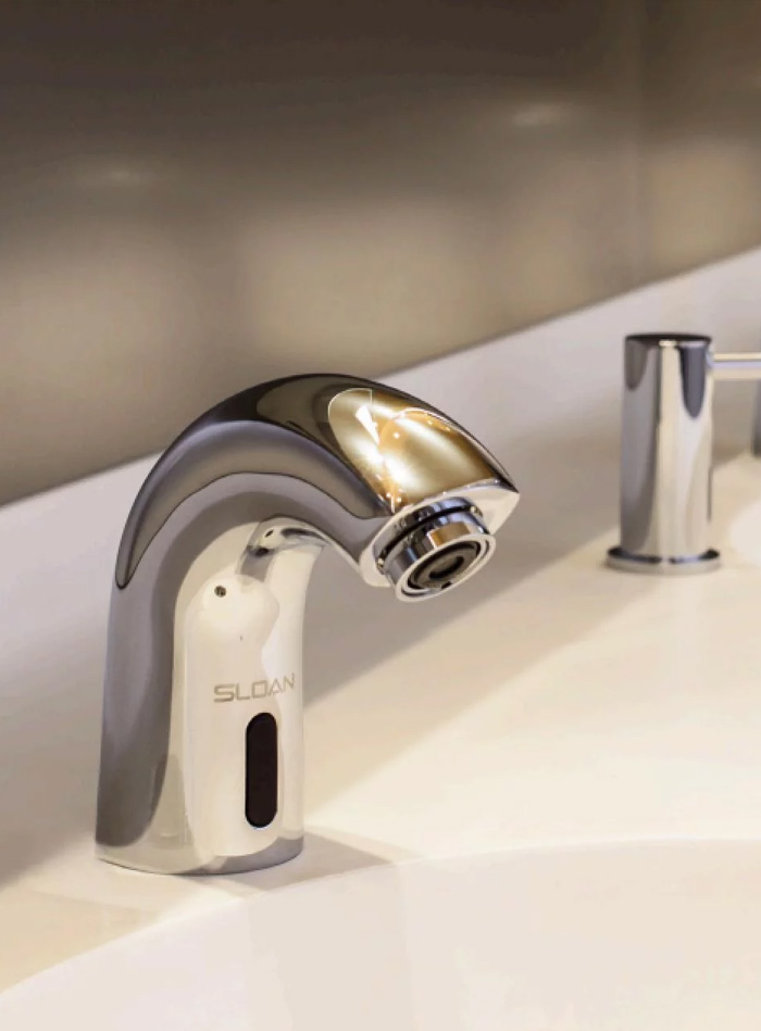 a row of Sloan automatic chrome faucets installed on a sleek white countertop. Their modern design and perfect alignment convey functionality, hygiene, and elegance—ideal for contemporary commercial or institutional spaces.