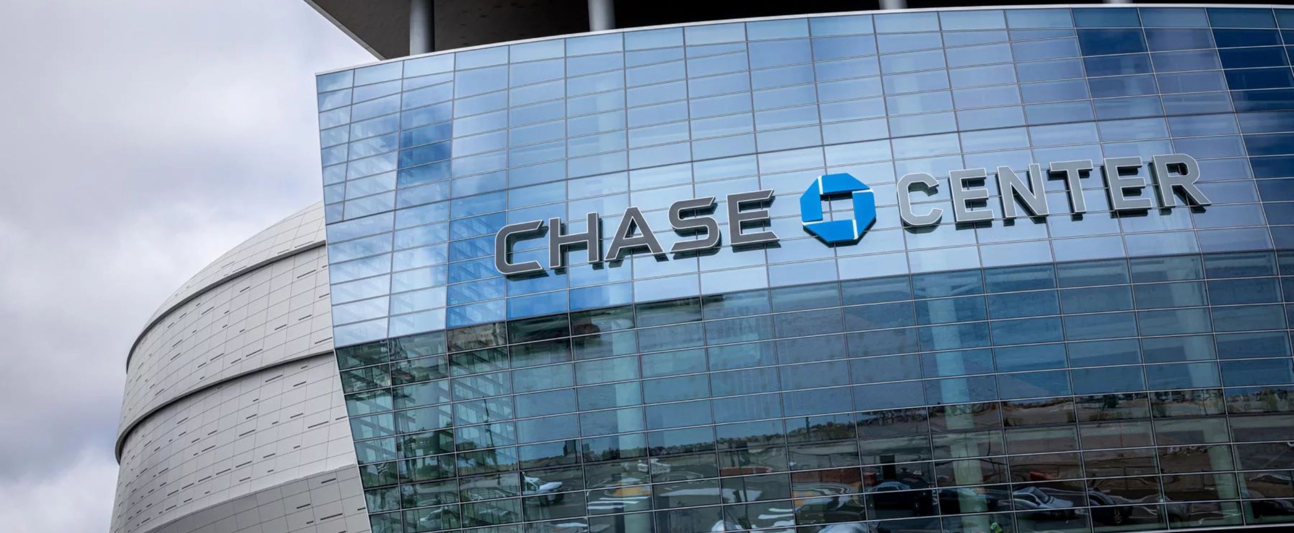 Exterior view of the Chase Center in San Francisco, featuring modern architecture and a distinctive curved glass façade reflecting the urban surroundings.
