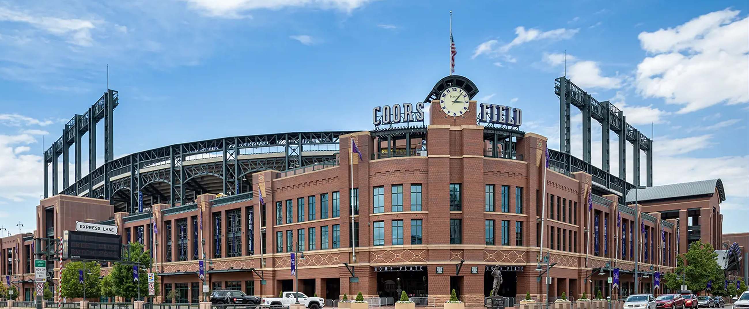 Coors Field, the iconic baseball stadium located in Denver, Colorado, home of the Colorado Rockies of Major League Baseball (MLB). Its red brick façade blends classic architecture with modern steel framing, reflecting the industrial character of Denver’s LoDo district. A large clock and the stadium’s name sign stand prominently above the main entrance, serving as distinctive architectural landmarks.