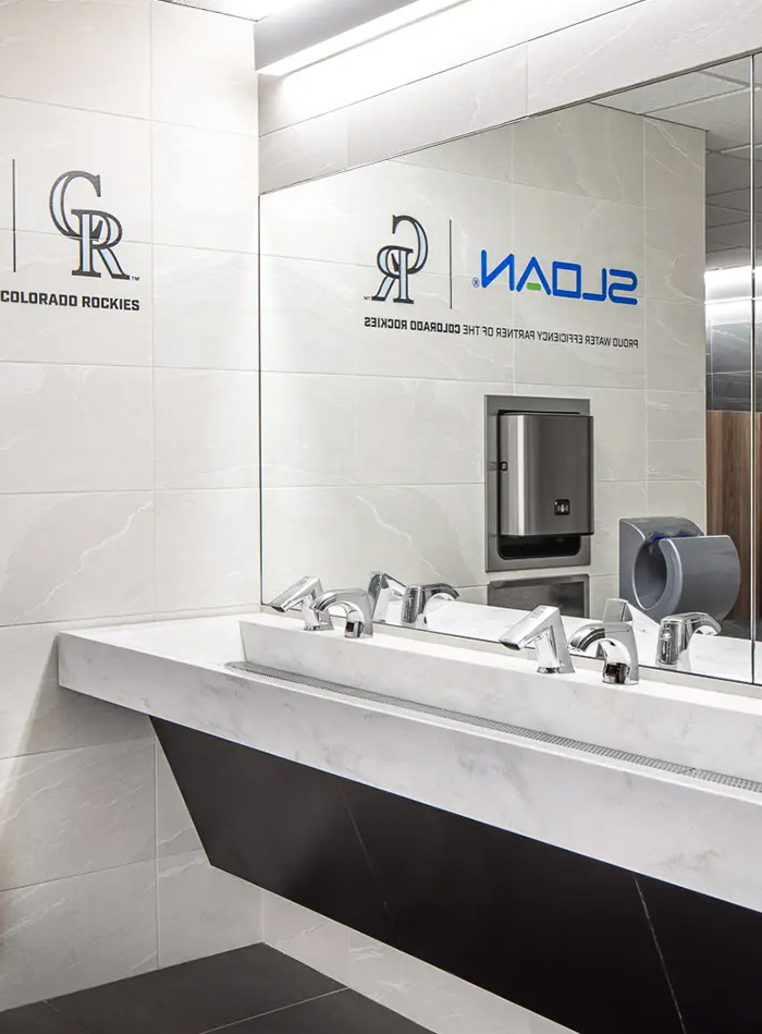 modern Sloan sink station installed in the restrooms at Coors Field, home of the Colorado Rockies. The design features white marble surfaces with black accents, offering a sleek and sophisticated appearance. The team’s logo and Sloan’s branding are visible on the mirror