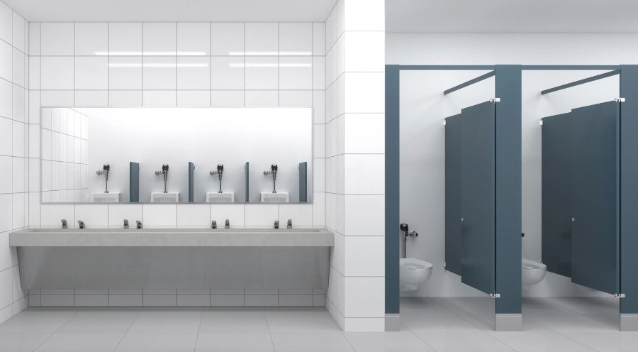 Baño público moderno con lavabos alineados frente a un gran espejo y puertas de casetas azules, diseñado para espacios educativos o institucionales.