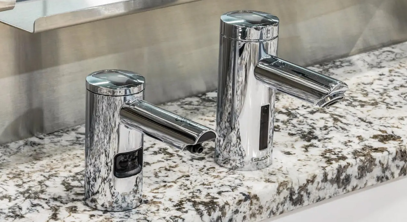 a Sloan faucet and soap dispenser system with automatic sensors, installed on a polished granite countertop. The cylindrical chrome finish design blends elegance with functionality, ensuring a touch-free hygienic experience.