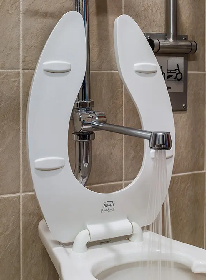 a public-use toilet designed for accessibility, featuring stainless steel side grab bars and a manual chrome flushometer. The setting, with beige tile walls, conveys cleanliness and functionality, ideal for institutional or commercial spaces.