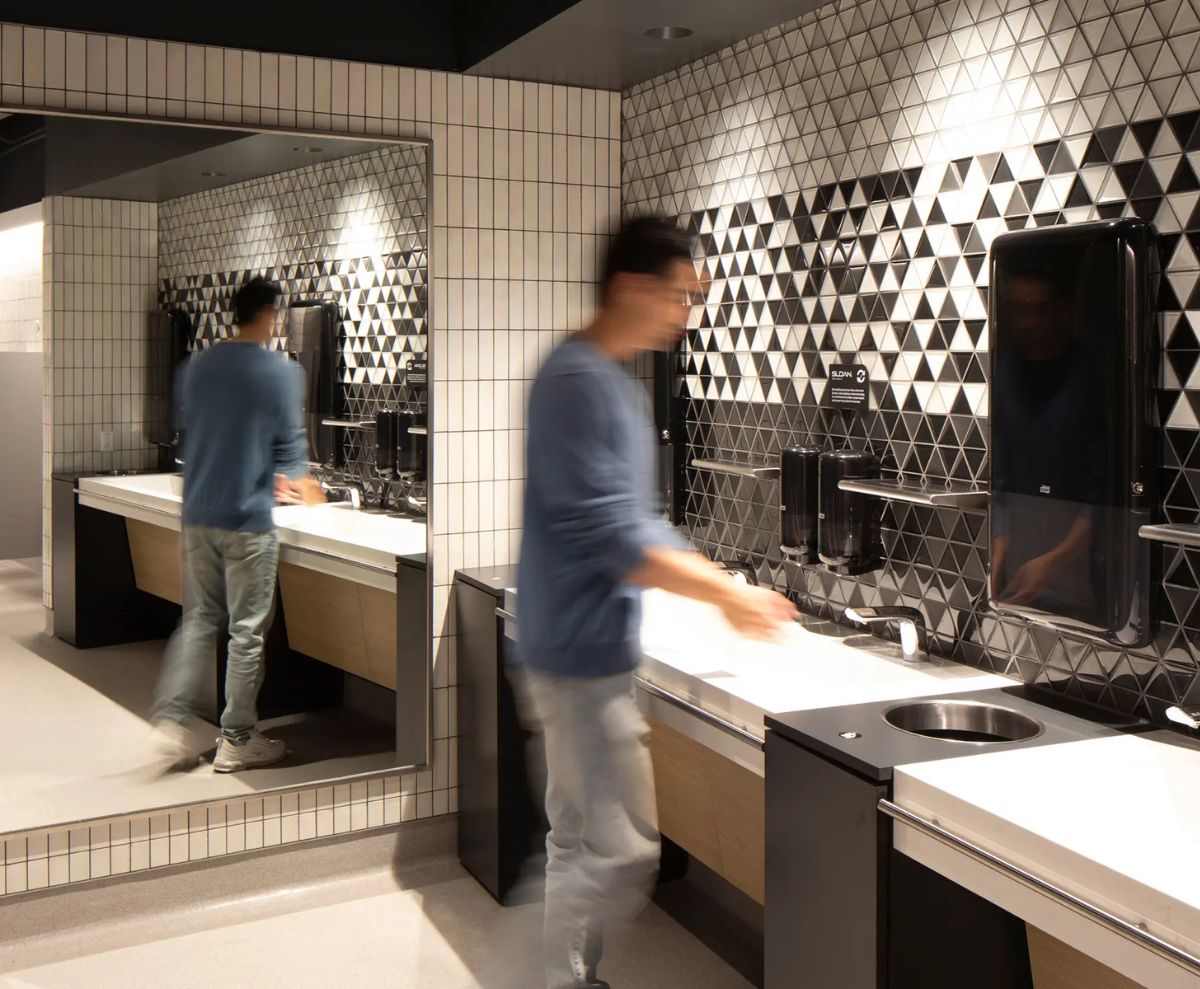 Person using the sink in a modern restroom with a black-and-white triangular tile wall, warm lighting, and automatic fixtures.