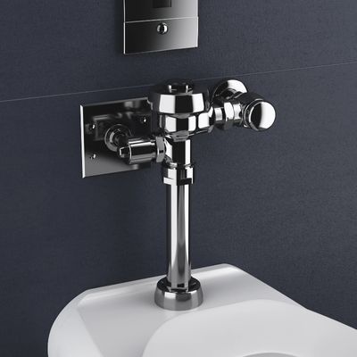 Exposed Sloan flushometer in polished chrome finish installed above a toilet against a dark blue wall with a recessed control plate.