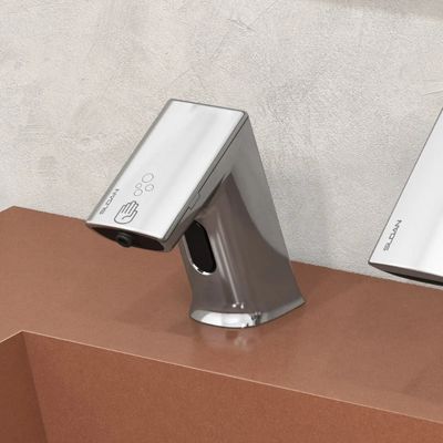 Sloan automatic soap dispenser in chrome finish, installed on a terracotta-colored countertop with a light gray textured wall.