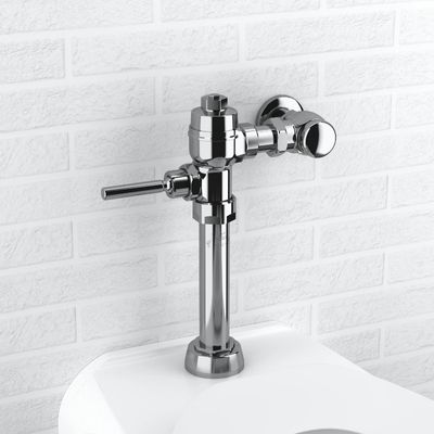 Sloan manual flushometer in polished chrome finish installed above a toilet against a white brick wall.