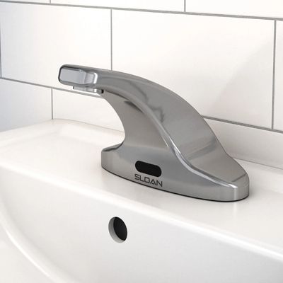 Sloan low-profile automatic chrome faucet installed on a white sink with rectangular white tile backsplash.