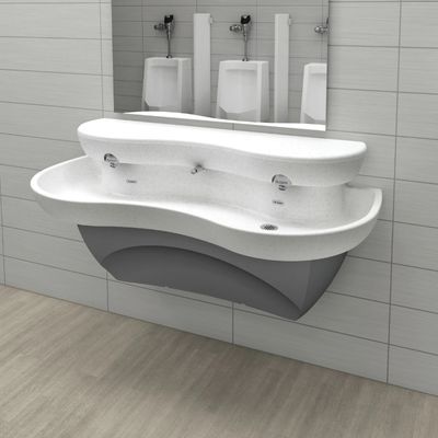 Lavabo blanco de superficie sólida con diseño curvo y dos grifos automáticos Sloan, frente a un espejo que refleja mingitorios al fondo.