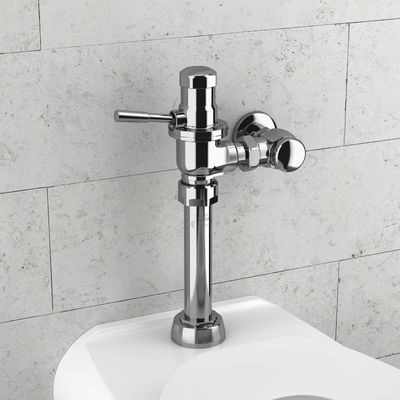 Sloan manual flushometer in polished chrome finish installed above a toilet against a light gray stone wall.