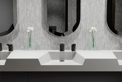 a contemporary Sloan® sink with a geometric design and neutral finishes. Each station includes black automatic faucets and soap dispensers, creating a sleek and modern look