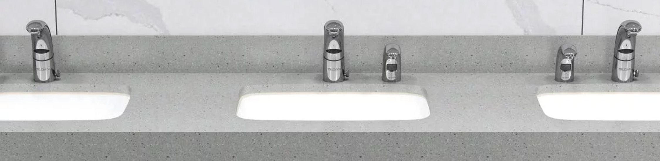 a row of sinks with Sloan® electronic faucets, set in a light-gray solid surface countertop.