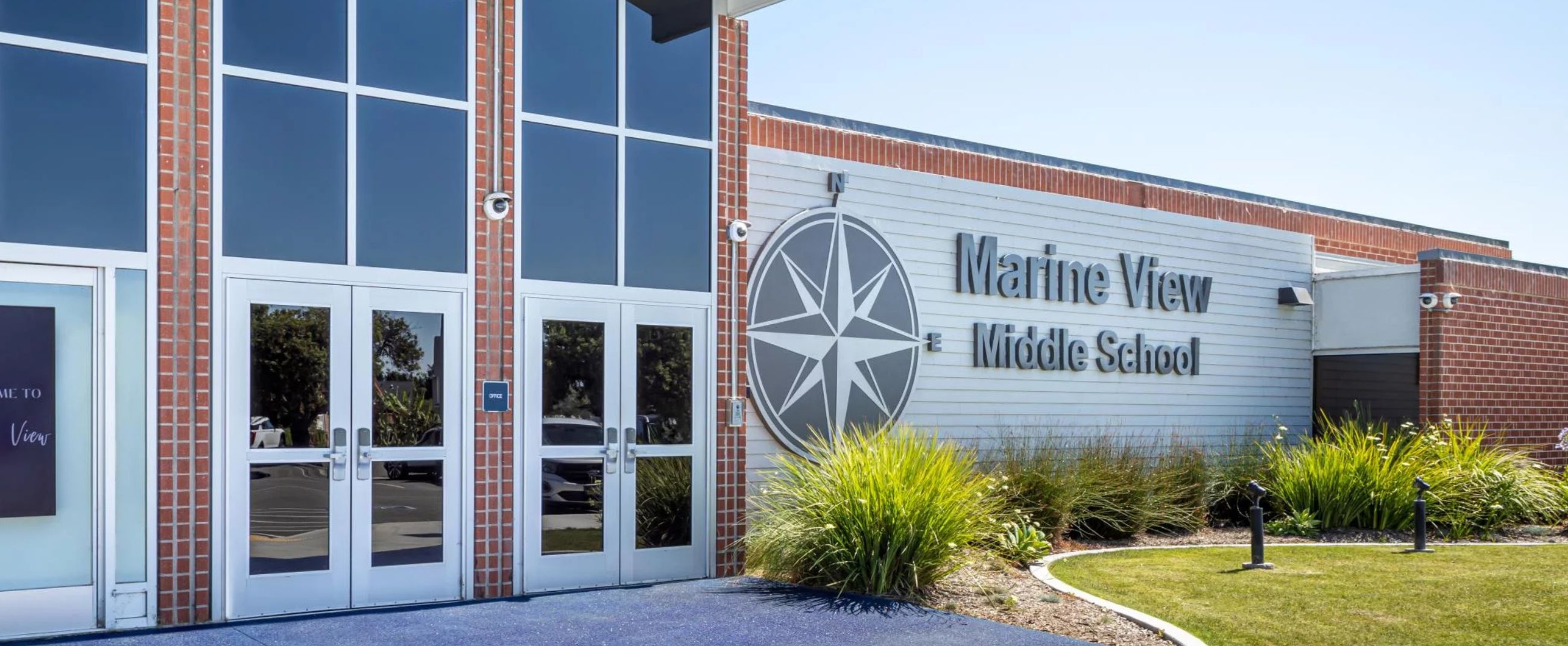 Main entrance of Marine View Middle School featuring modern architecture, red brick, and the Ocean View School District compass emblem symbolizing direction and learning.