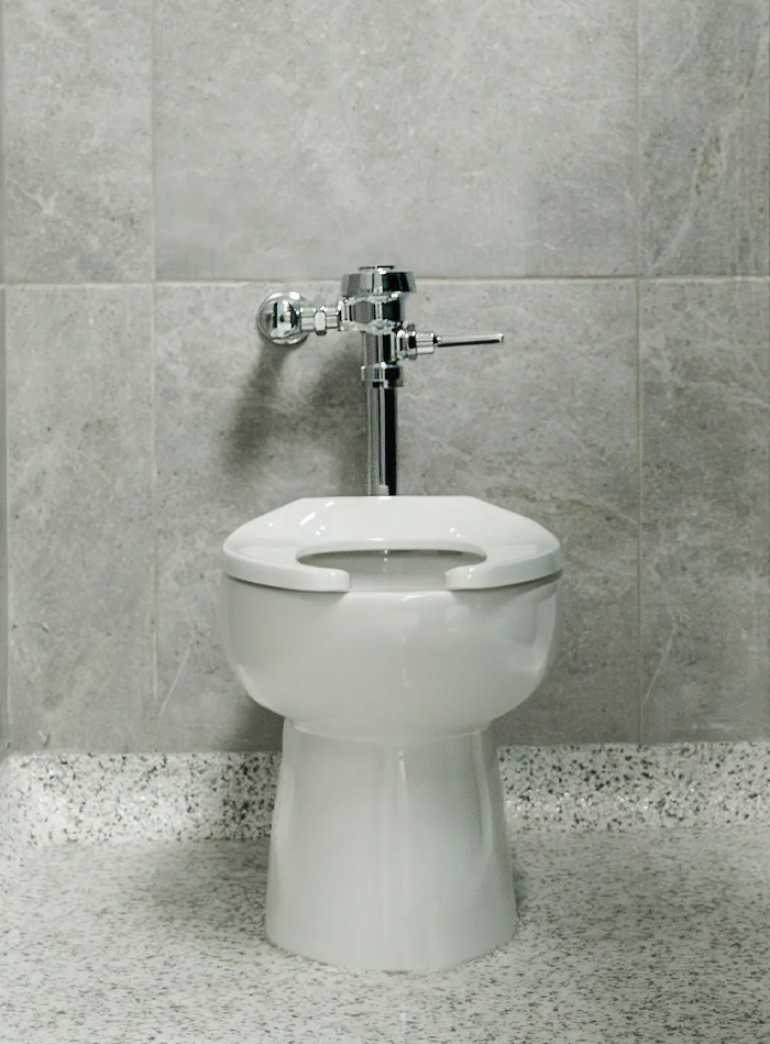an individual restroom stall with light gray tiled walls and metallic blue doors. The space appears clean and modern, featuring durable finishes and a functional design that emphasizes hygiene and privacy.