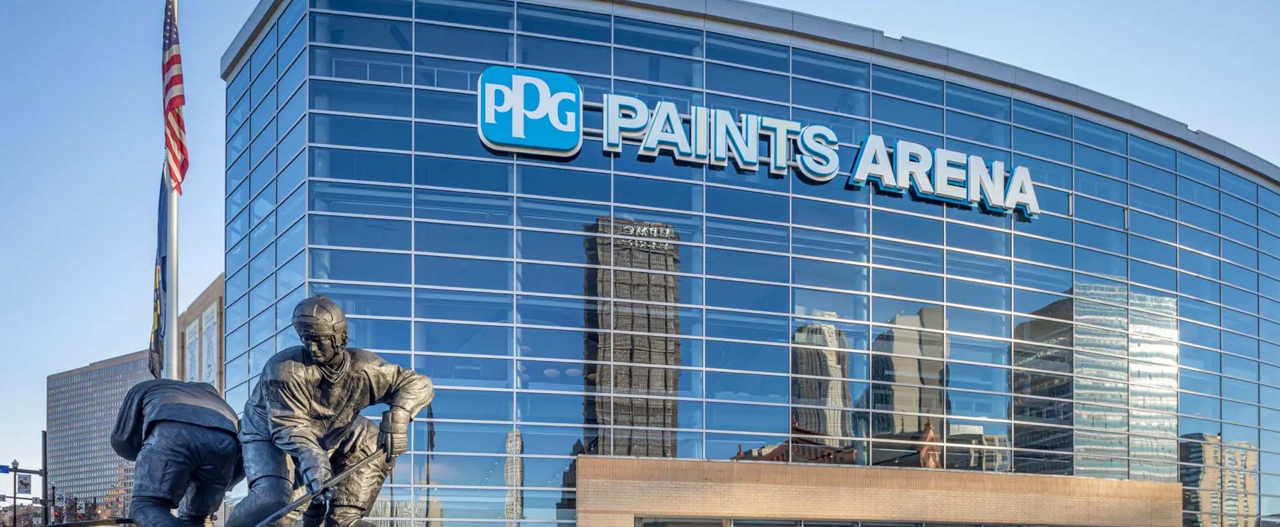 impressive façade of PPG Paints Arena in Pittsburgh, Pennsylvania, a modern venue known for hosting sports events, concerts, and large-scale performances. Its curved glass and steel structure reflects the city skyline, while the statues at the entrance pay tribute to hockey, one of Pittsburgh’s most iconic sports.