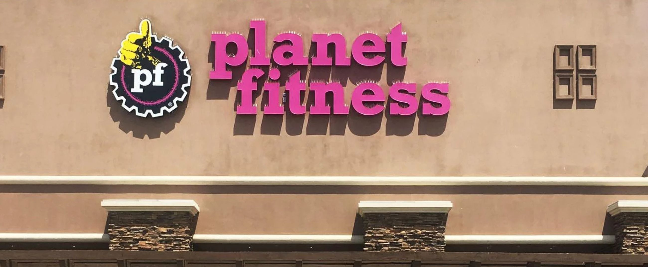 Exterior facade of a Planet Fitness gym featuring its iconic purple and yellow logo, symbolizing wellness and positive energy.