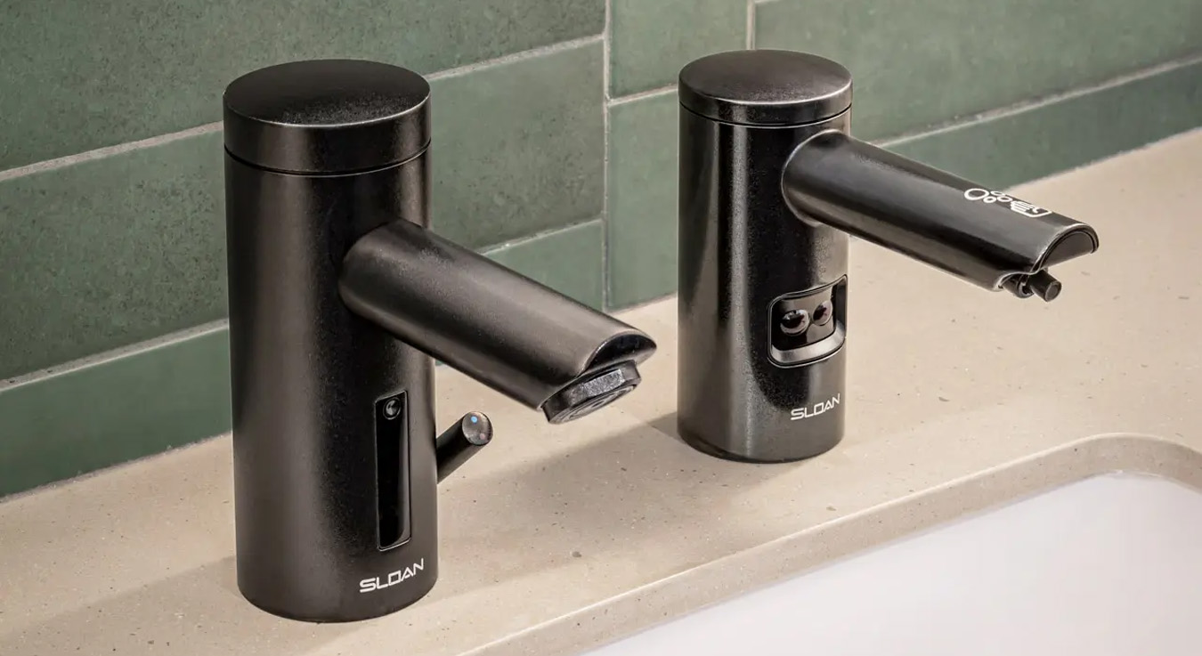 Sloan automatic faucet and a matching soap dispenser, both in a matte black finish, installed on a light beige countertop against a green tiled wall. Each device features integrated sensors for touch-free operation, emphasizing hygiene and efficiency.