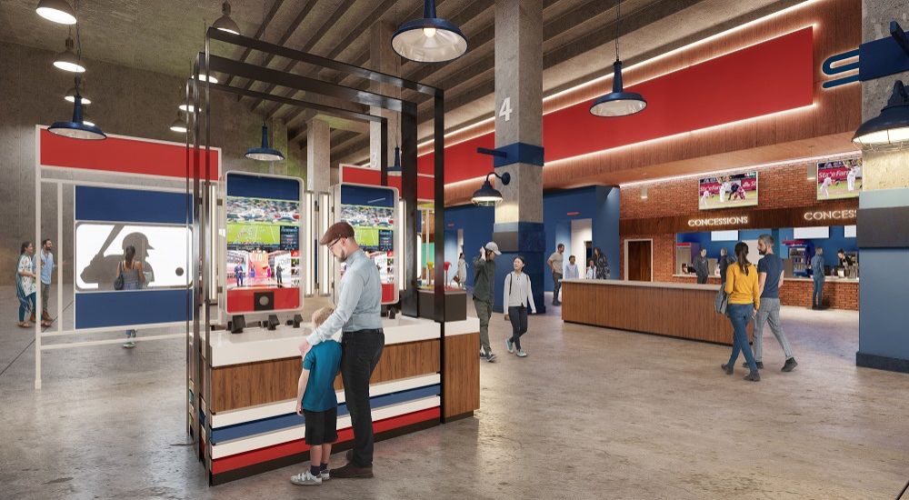 Concession area in a sports stadium with a modern design featuring red, blue, and wood tones, where people are purchasing food and drinks.