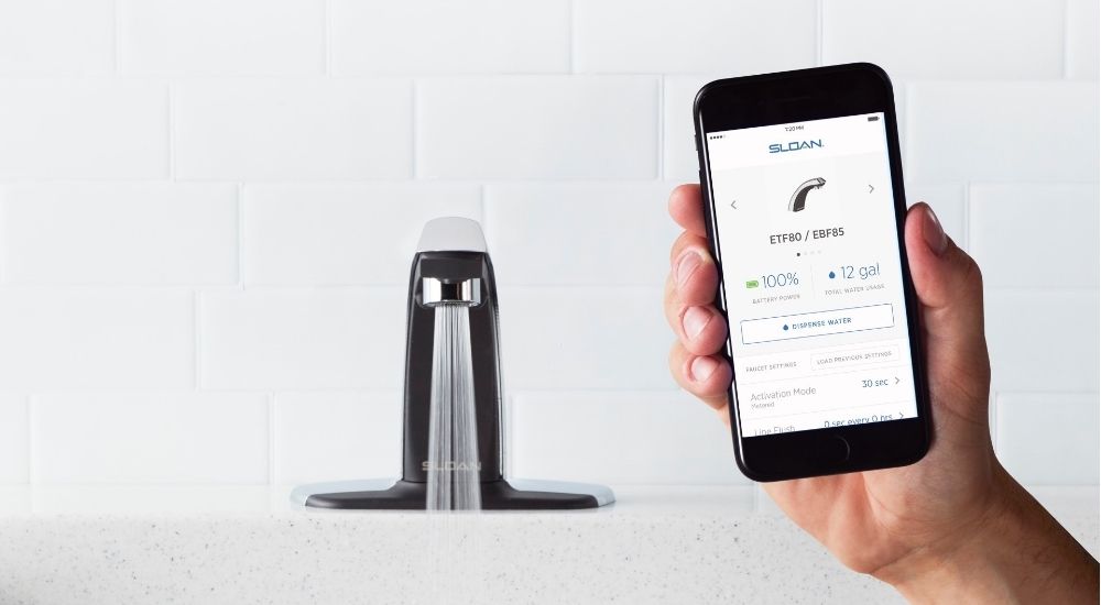 Hand holding smartphone with Sloan app controlling touchless faucet
