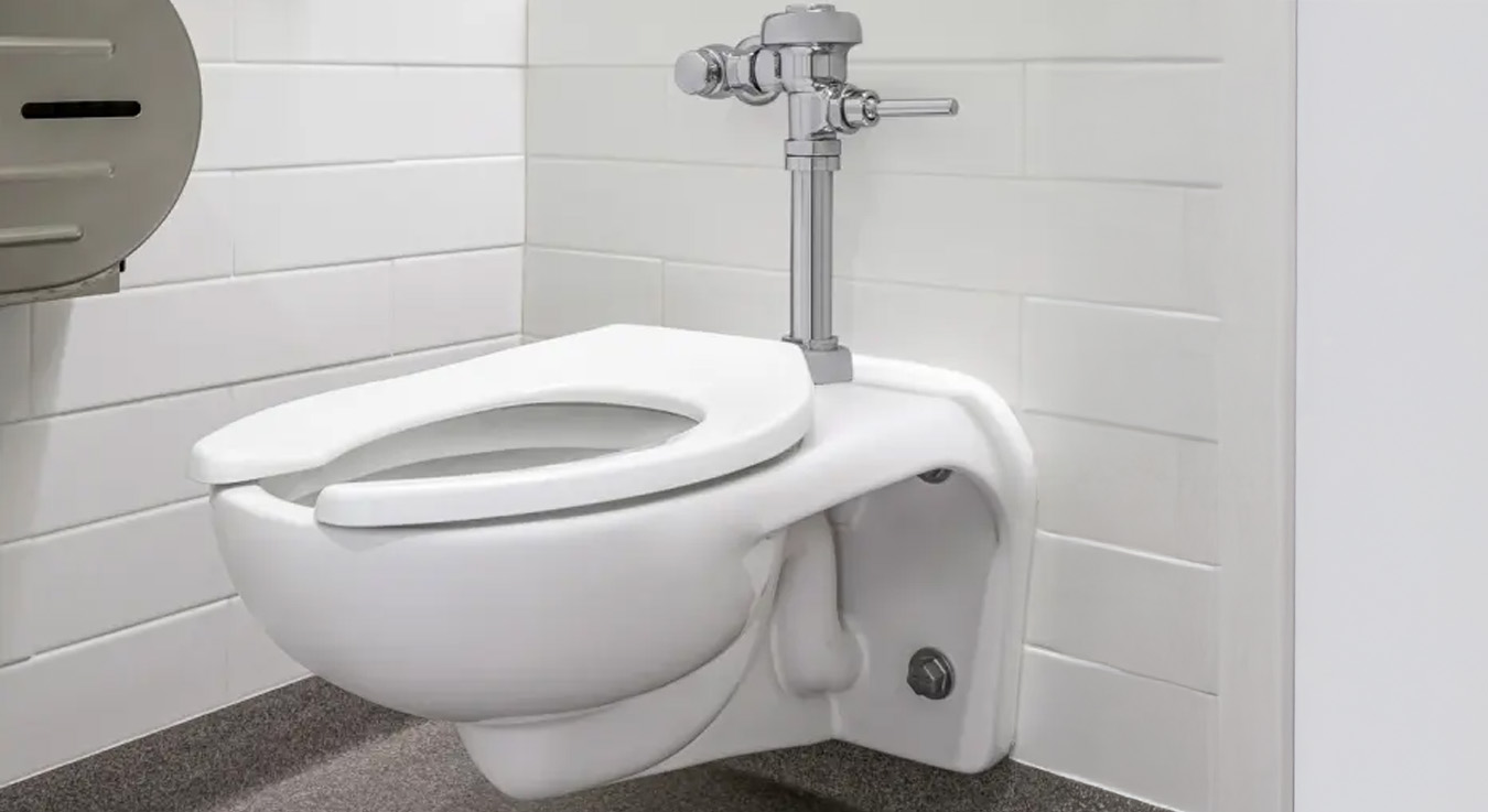 a wall-mounted toilet with a manual Sloan flushometer, designed for institutional or educational use. Its suspended installation maximizes floor space and simplifies cleaning, while the chrome-plated flushometer adds a modern and durable touch.