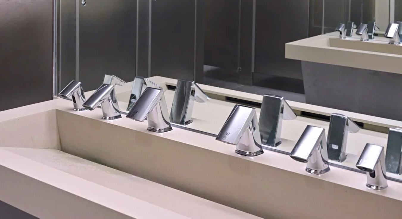 instalación de lavabos múltiples con grifos electrónicos Sloan, cada uno con sensor de activación y diseño angular en acabado cromado. El conjunto refleja un entorno moderno, higiénico y eficiente, donde la tecnología sin contacto contribuye al ahorro de agua y a la reducción de contagios por contacto.