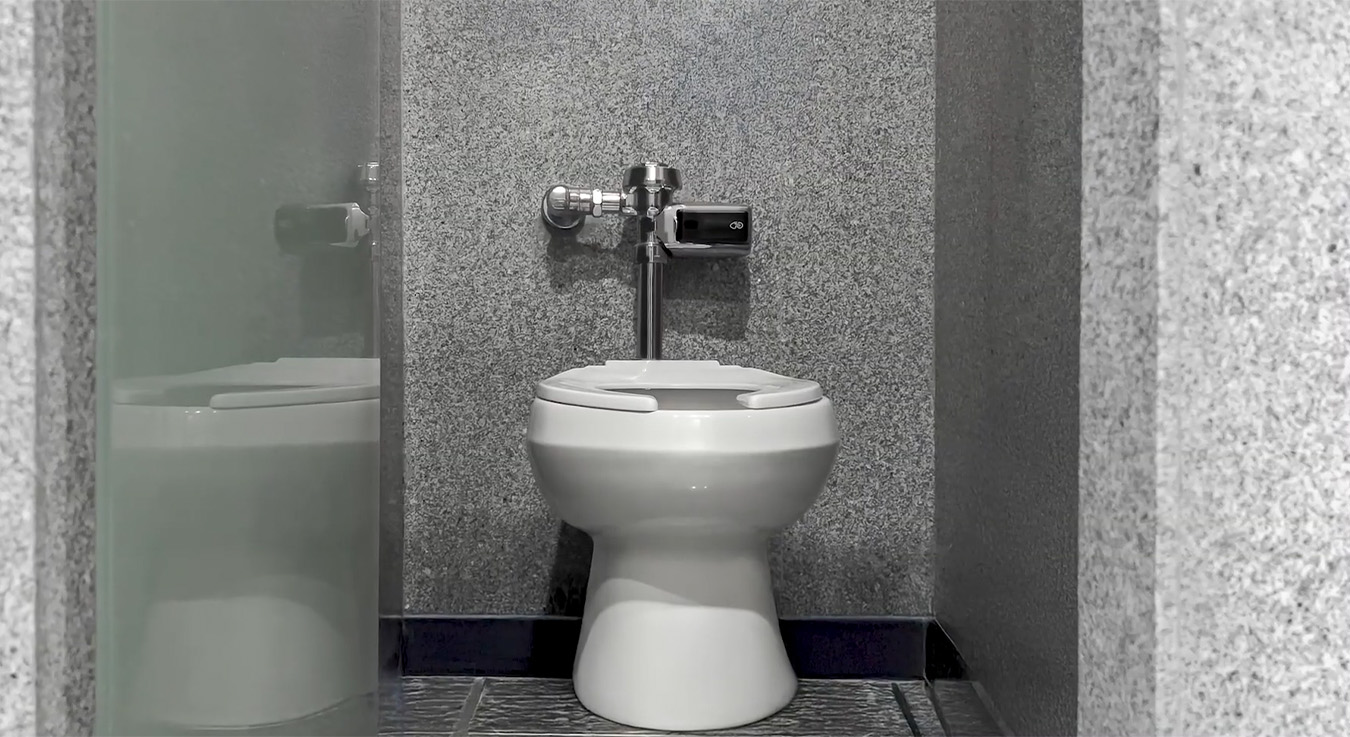 a modern toilet with gray granite walls and a chrome automatic sensor flush valve. The design is minimalist and functional, emphasizing cleanliness, material durability, and the use of technology for a more hygienic and efficient experience.
