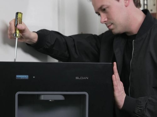 Técnico usando un destornillador para realizar mantenimiento en un dispensador de agua negro empotrado.