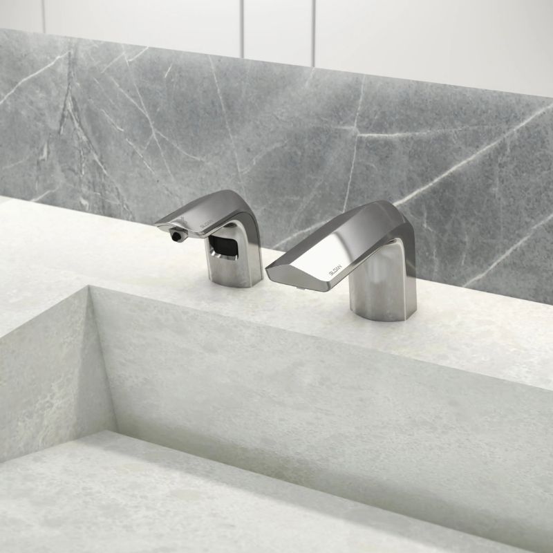 Sloan automatic faucet and soap dispenser in polished chrome finish installed on a light stone countertop with a gray marble backsplash.