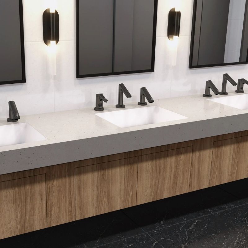 Modern sinks with Sloan automatic faucets and soap dispensers in matte black finish, installed on a solid surface countertop with wood cabinetry and side-lit mirrors.