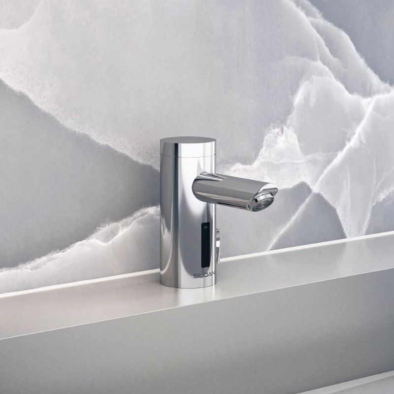 Sloan automatic chrome faucet with cylindrical body, mounted on a gray countertop with a light gray marble-patterned wall.