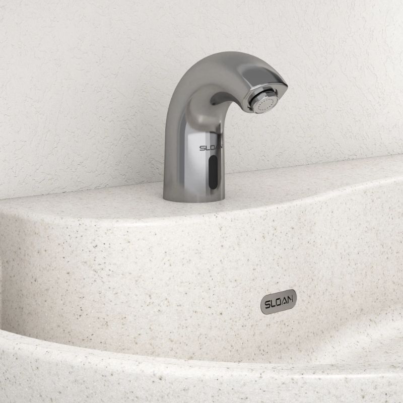 Sloan automatic chrome faucet with curved design, installed on an ivory solid surface countertop with a textured wall background.