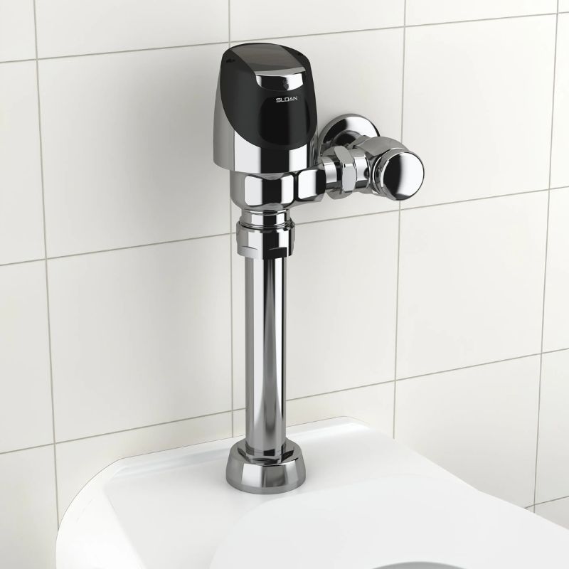 Sloan automatic flushometer in polished chrome finish installed above a toilet against a light beige tiled wall.