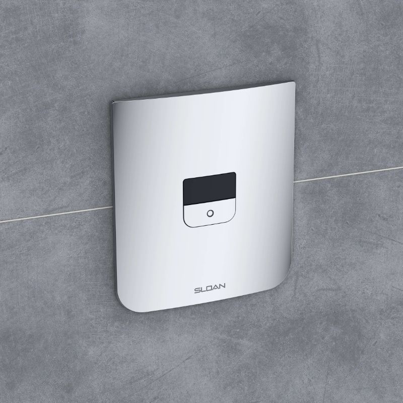 Sloan sensor plate for concealed flushometer in polished chrome finish mounted on a gray marble wall.
