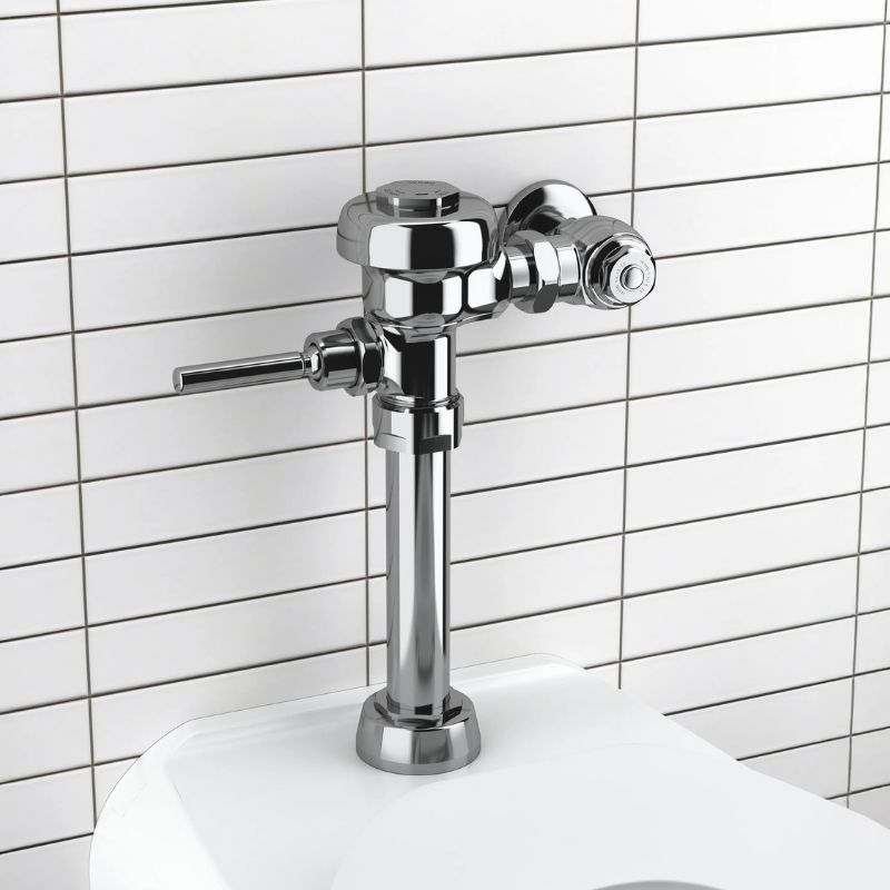 Sloan manual flushometer in polished chrome finish installed above a toilet against a white rectangular tile wall.