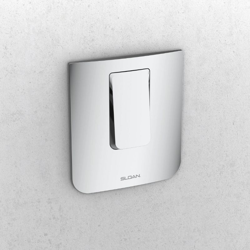 Sloan manual push-button plate for concealed flushometer in polished chrome finish mounted on a light gray wall.