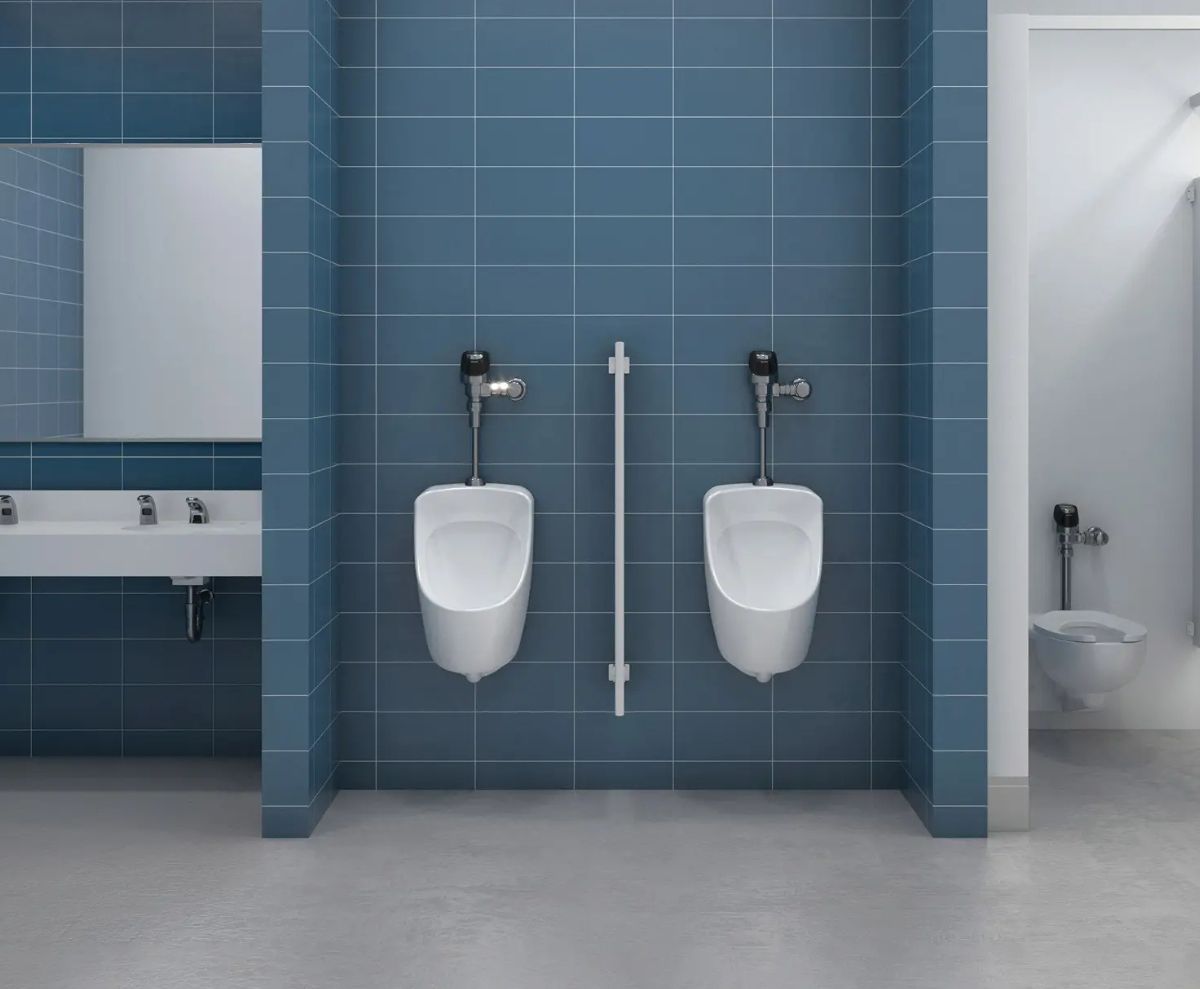 Baño público con urinarios automáticos y paredes de azulejos azules, que incluye lavabos y una cabina accesible al fondo, diseñado para espacios institucionales.