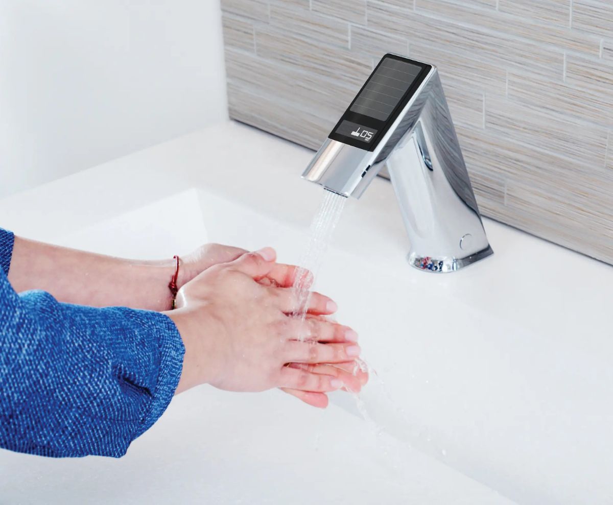 Persona lavándose las manos bajo un grifo con sensor alimentado por energía solar, diseñado para promover la higiene y la eficiencia energética en espacios modernos.