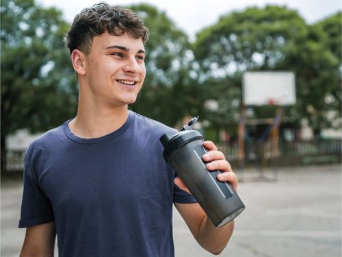 Joven sosteniendo una botella reutilizable en una cancha al aire libre, promoviendo una hidratación sostenible.