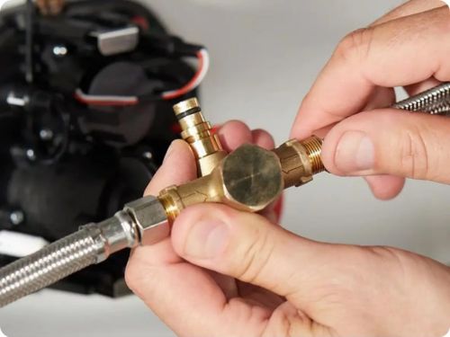 Manos de una persona instalando una válvula o conector de latón con mangueras metálicas, parte de un sistema de control para grifo automático.