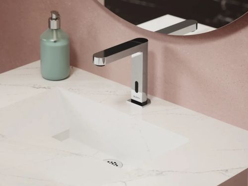 Grifo automático de diseño cuadrado sobre un lavabo de mármol blanco, acompañado de un dispensador de jabón verde.