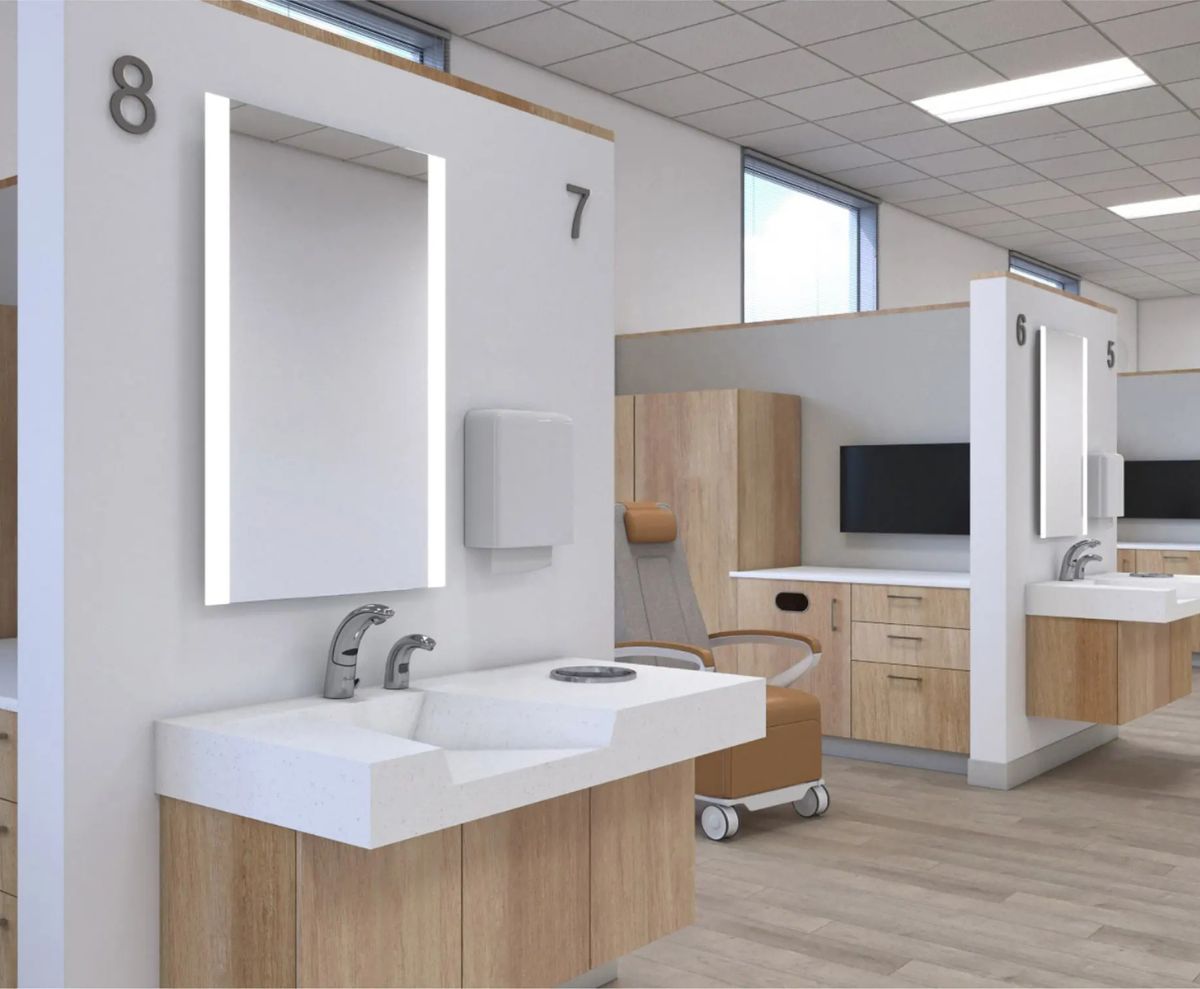 Área de atención médica moderna con lavabos de superficie sólida, grifos automáticos, espejos con iluminación LED y gabinetes de madera clara.
