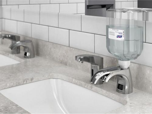 Lavabos con grifos automáticos y dispensadores de jabón de llenado superior instalados sobre una encimera de superficie sólida en un baño moderno.
